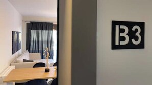Ein Hotelzimmer mit Bett, Schreibtisch, Stuhl, einem Fenster mit Vorhängen und einem an der Wand befestigten Schild mit der Aufschrift 'B3'.