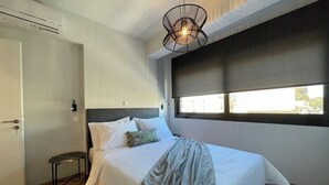 Ein Schlafzimmer mit einem Bett, einem Fenster mit Jalousien, einer Tür und einem kleinen Tisch.