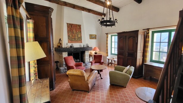 A room with a fireplace, red armchairs, a green armchair, a wooden table, and a staircase. - In a quiet, green setting, pretty Provencal country house (Annot)