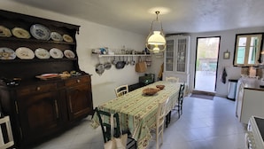 A kitchen with a dining table, chairs, a hanging light fixture, and a window. - In a quiet, green setting, pretty Provencal country house (Annot)