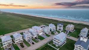 Et kystnært boligområde med huse langs stranden, bestående af både etage- og parcelhuse, fri udsigt over havet og en velplejet græsplæne.