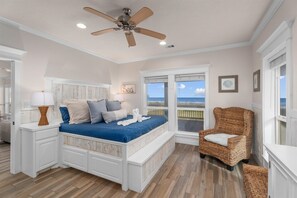 Ein Schlafzimmer mit Bett, Sessel, Fenster mit Blick, Deckenventilator und einem Wandbild.