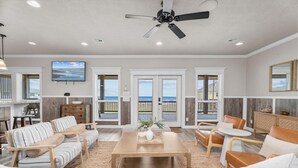 A spacious living room with a wooden coffee table, striped sofas, and a view of the ocean through large windows. - Beachfront | 6BR | Sleeps 33 | Hot Tub | Pickleball (Crystal Beach)