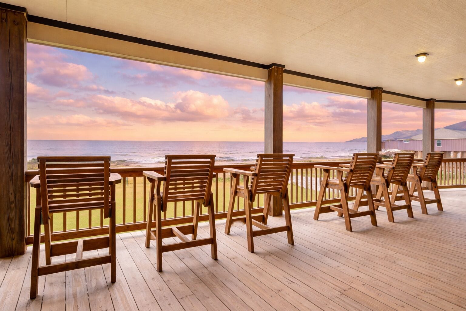 A covered outdoor seating area with wooden chairs and a view of the ocean.