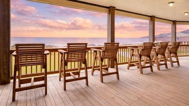 A covered outdoor seating area with wooden chairs and a view of the ocean. - Beachfront | 6BR | Sleeps 33 | Hot Tub | Pickleball (Crystal Beach)