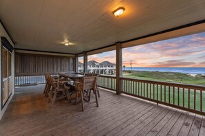 Ein überdachter Außenbereich mit Holztisch und -stühlen, einer Brüstung und Blick auf das Meer und Gebäude im Hintergrund.