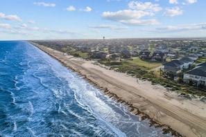 An aerial view of a coastal residential area with houses, a beach, and a distant water tower. - Beachfront | 6BR | Sleeps 33 | Hot Tub | Pickleball (Crystal Beach)