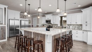 A modern kitchen with white cabinets, a large island with stools, stainless steel appliances, and pendant lighting. - Beachfront | 6BR | Sleeps 33 | Hot Tub | Pickleball (Crystal Beach)