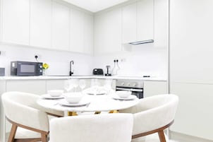 Una cocina moderna con armarios blancos, una mesa de comedor con vajilla blanca y un microondas en la encimera.
