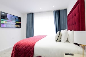 Una habitación de hotel con una cama, un televisor en la pared y cortinas.