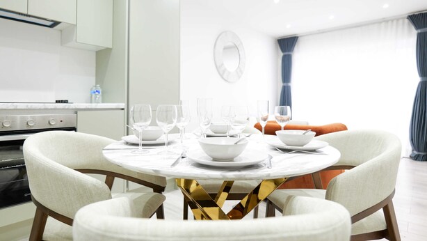 Zona pranzo con tavolo rotondo, sedie bianche e una cucina sullo sfondo.