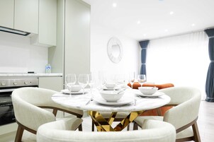 Un comedor con una mesa redonda, sillas blancas y una cocina al fondo.