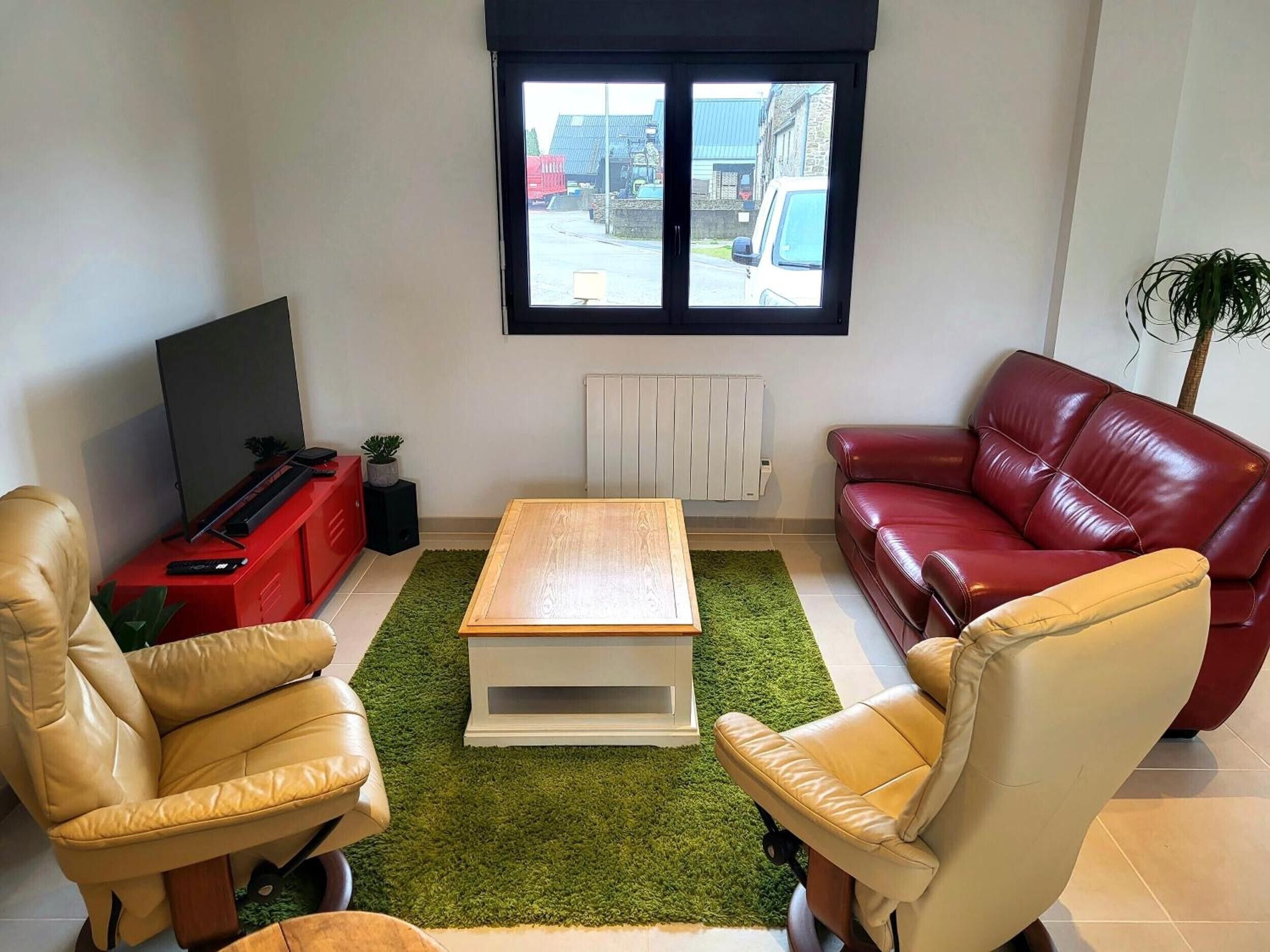 A living room with a television, red leather sofa, beige leather armchair, and a small table.