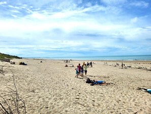 Une vaste plage de sable où l’on voit des gens se promener et s’asseoir, et un ciel dégagé au-dessus.