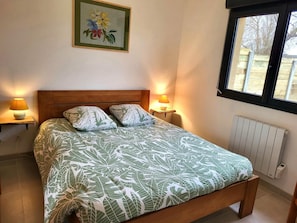 Une chambre à coucher avec un lit en bois, deux lampes de chevet, un radiateur et une fenêtre donnant sur des arbres.