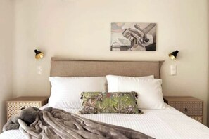 Ein Bett mit Kopfteil, zwei Nachttischlampen, ein Nachttisch und ein an der Wand hängendes Kunstwerk.