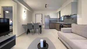 Una sala de estar moderna con televisor de pantalla plana, un sofá, zona de comedor con sillas y cocina con armarios y electrodomésticos.