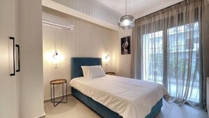 Un dormitorio con cama, mesitas de noche, lámpara colgante y ventana con cortinas.