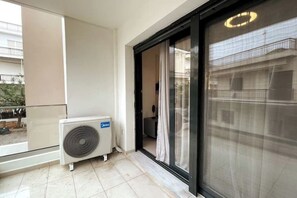 Un balcon doté d’un grand climatiseur, d’une porte-fenêtre coulissante et offrant une vue sur un immeuble situé de l’autre côté de la rue.