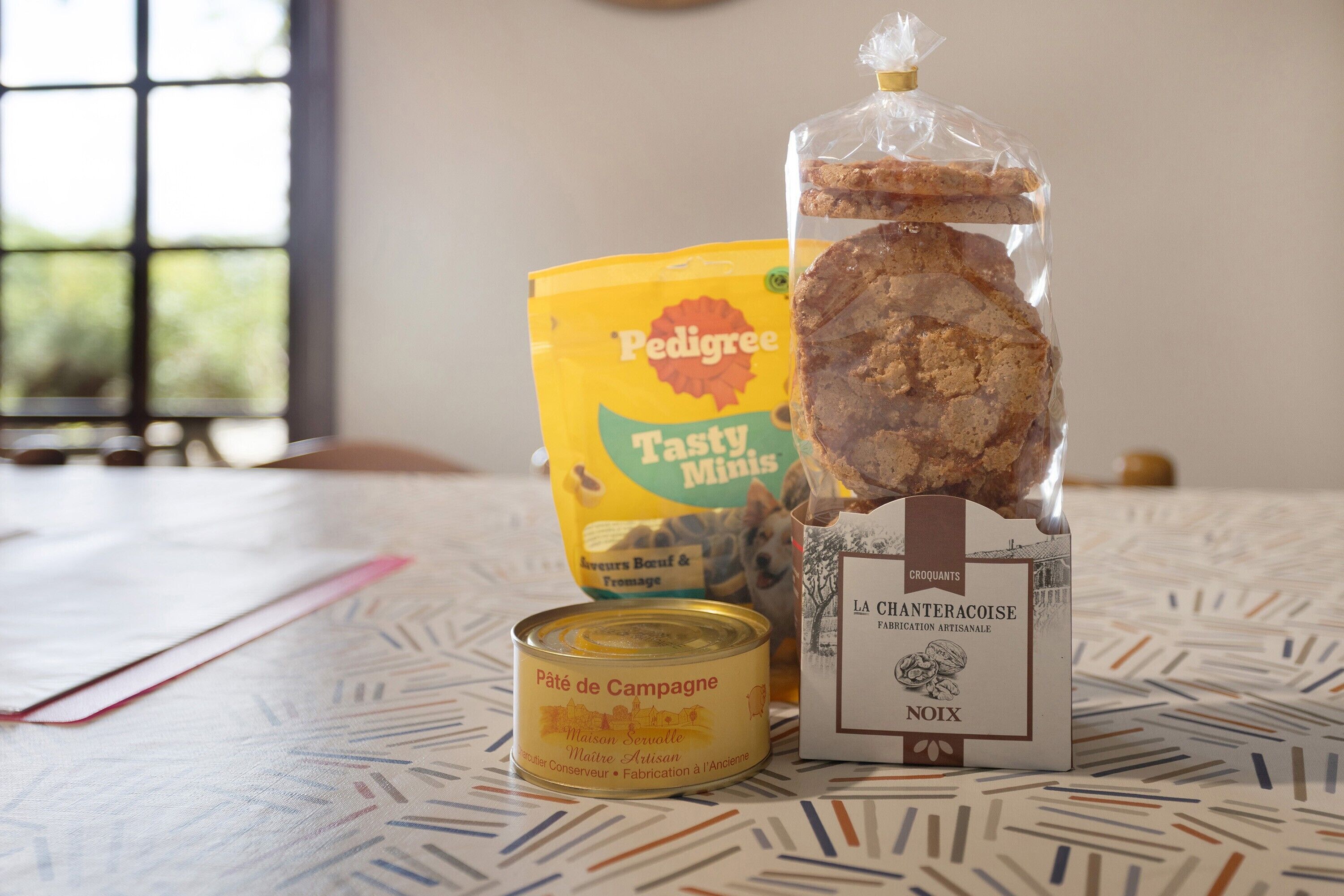 Una mesa con una lata de paté campestre, una bolsa de Pedigree Tasty Minis y un paquete de croquants.