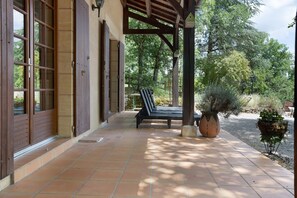 Eine überdachte Terrasse mit einer Bank, einem großen Topfpflanzen und einer Holzpergola.