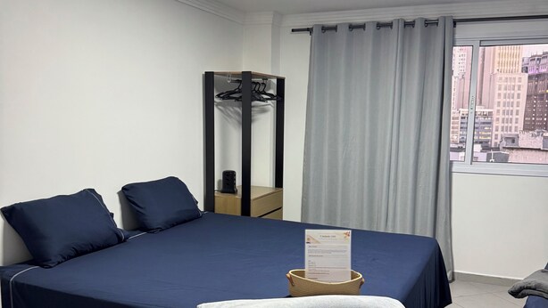 Een hotelkamer met een bed, een spiegel, een raam met gordijnen en uitzicht op de stad.