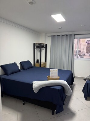 Ein Hotelzimmer mit Bett, Spiegel, Fenster mit Vorhängen und Blick auf die Stadt.