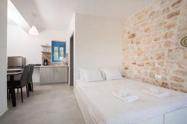 A bedroom with a bed, a desk, and a kitchenette.