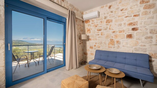 A room with a stone wall, a blue sofa, a table with two bowls, a pair of chairs, and a sliding glass door leading to a balcony.