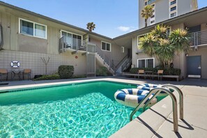 A swimming pool with a clear blue water surface, surrounded by a patio area with outdoor seating and a staircase leading to an upper level. - The Beach Bungalow | Ocean Front (San Diego)