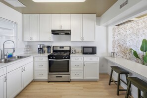 A modern kitchen with white cabinets, stainless steel appliances, and a wooden floor. - Sea Cliff #8 | La Palma (San Diego)
