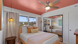 Une chambre à coucher avec un lit, un ventilateur de plafond, de grandes fenêtres et une vue sur l’extérieur.
