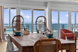 A wooden dining table with chairs, a view of the ocean, and large windows. - The Cabana | ocean front & pool (San Diego)