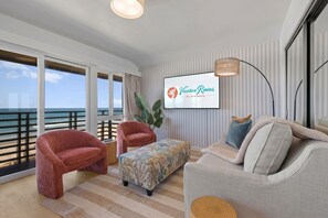 A modern living room with a large window overlooking the ocean, a flat-screen TV, and a cozy seating area with a sofa and armchairs. - The Cabana | ocean front & pool (San Diego)