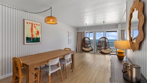 Un coin repas avec une table et des chaises en bois, un fauteuil suspendu, une lampe et un grand miroir.