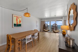 Un coin repas avec une table et des chaises en bois, un fauteuil suspendu, une lampe et un grand miroir.