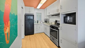 Une cuisine moderne avec des meubles blancs, un réfrigérateur noir, une cuisinière et un four à micro-ondes.