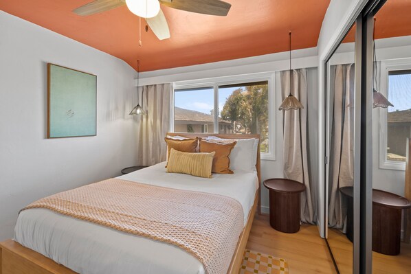 A bedroom with a bed, a ceiling fan, a window with curtains, and a view of the outside. - The Cabana | ocean front & pool (San Diego)