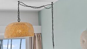 Ein Zimmer mit einer hängenden gewebten Leuchte, einem Fenster mit Vorhängen und einer Wand mit strukturierter Dekoration.