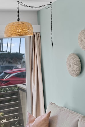 A room with a hanging woven light fixture, a window with curtains, and a wall with textured decor. - Seabreeze - Ocean Front (San Diego)