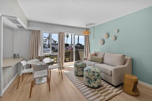 A modern living room with a sofa, ottomans, a dining table with chairs, and a view through a sliding door to an outdoor area. - Seabreeze - Ocean Front (San Diego)