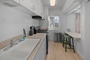A modern kitchen with a sink, stove, and stools. - Seabreeze - Ocean Front (San Diego)