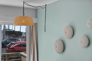 A room with a hanging woven light fixture, a window with a view of parked cars, and wall-mounted textured decorations. - Seabreeze - Ocean Front (San Diego)
