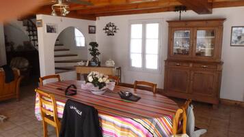 Un coin repas avec une table en bois, des chaises, une nappe à rayures, un vase avec des fleurs, un ventilateur de plafond et un buffet en bois.