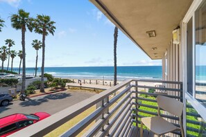 A balcony with a view of the beach, palm trees, and parked cars. - Good Vibes - Ocean Front (San Diego)