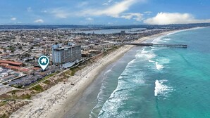 Luftaufnahme einer Küstenstadt mit Strand, einem Steg und einem Hotel mit Meerblick.
