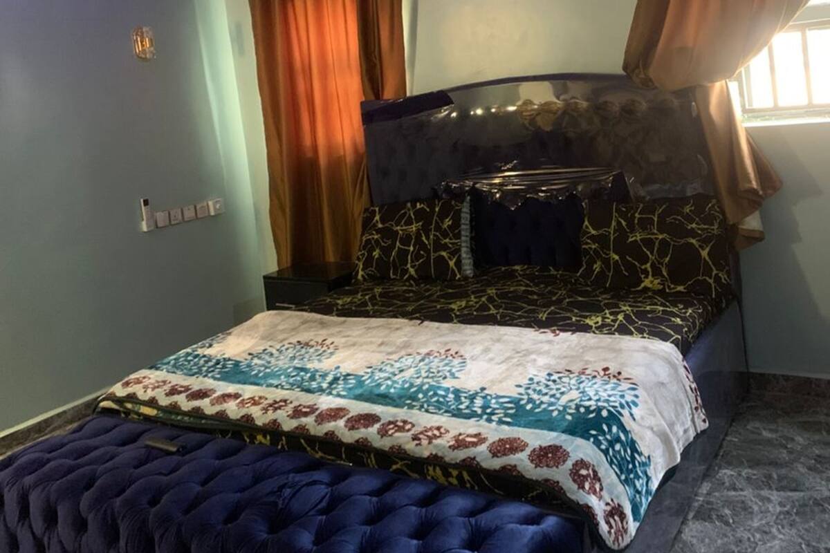 Een slaapkamer met een bed, een plafondventilator, een airconditioning en gordijnen.
