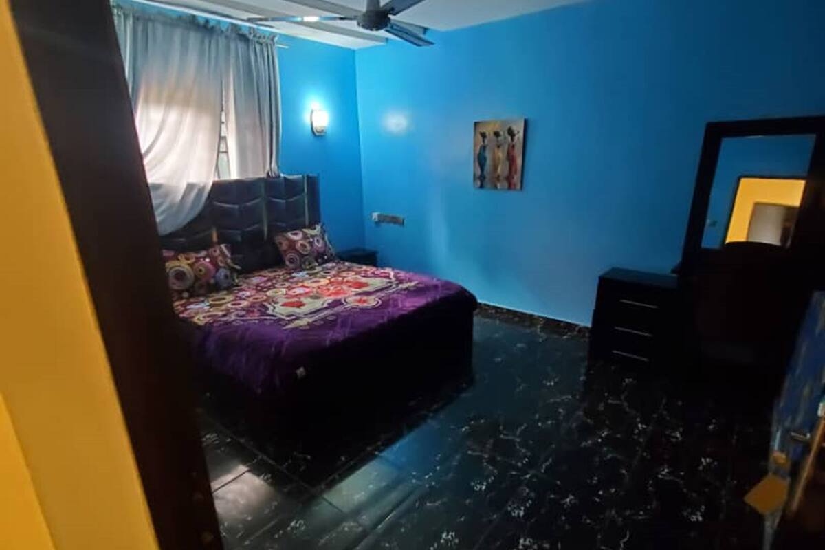 Een slaapkamer met een bed, een plafondventilator, een schilderij en een dressoir.