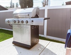 Una parrilla para exteriores de acero inoxidable, con tapa, cuatro perillas de control y un quemador lateral.