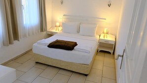 A neatly made bed with white linens and a brown towel, two bedside lamps, and a window with curtains.